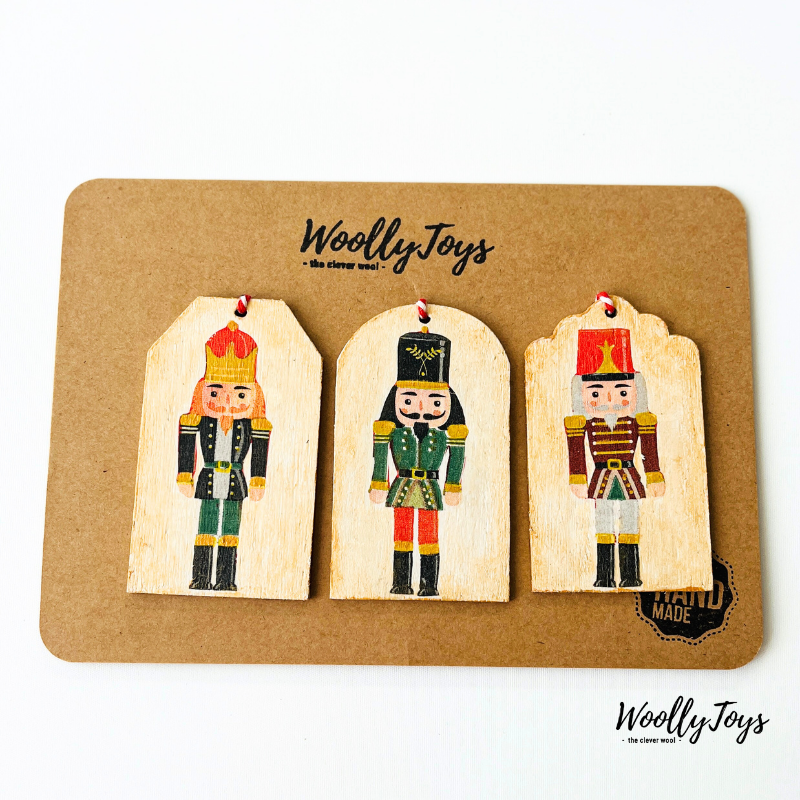 Három kézműves fa ajándékkísérő diótörő mintával, szalvéta technikával, natúr kraft karton csomagoláson, készen az ajándékozásra.