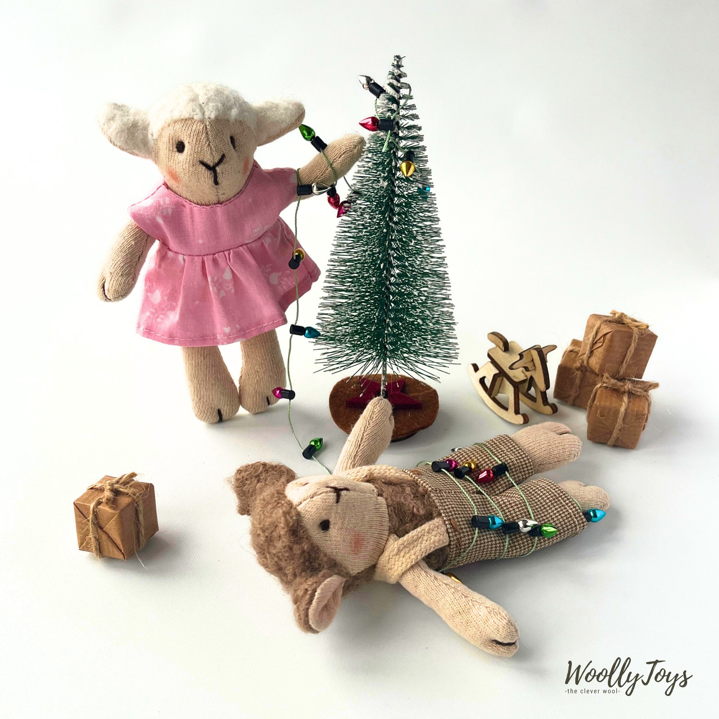 Gyapjúval töltött Felhőcske bárány figurák éppen díszítik a mini karácsonyfát, egyikük aki barna színű, kantáros, kockás nadrágot visel  a fényfüzérbe belegabalyodba fekszik a földön. A rószaszín kisruhában lévő fehér bárány figura az egyik kezével épp a fényfűzért rakja fel a karácsonyfára. Körülöttük ajándékdobozok és a fa hintaló. 