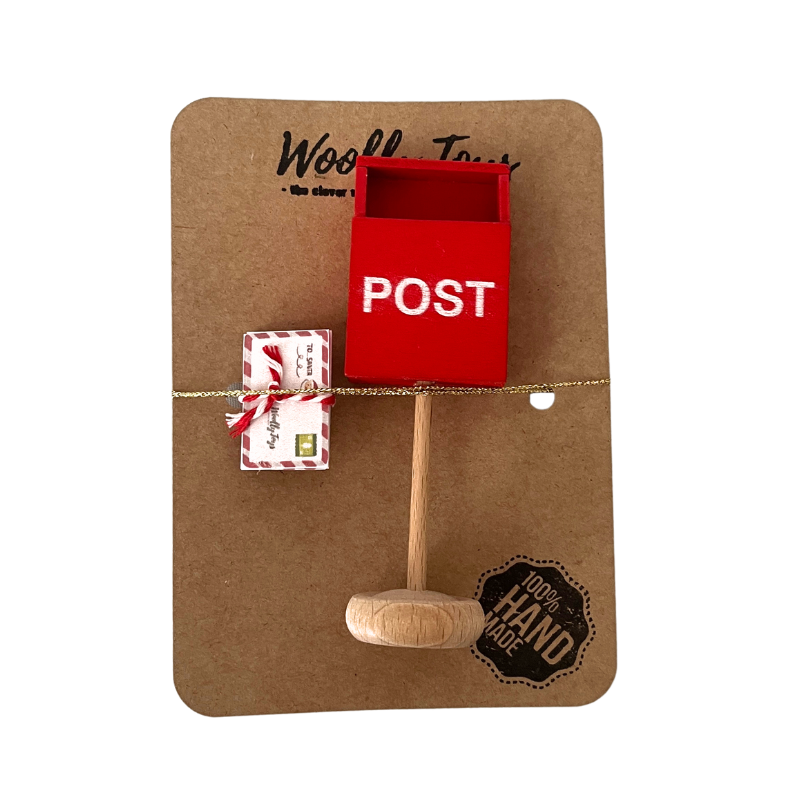 Kézműves természetes fa festett piros postaláda, fehér POST feliratt. Mellette 6 db Mikulásnak címzett színes kartonból készült levél csomag , melyek egy kraft barna színű papír karton csomagoláson vannak. A karton lap tetején WoollyToys felirat, a jobb alsó sarokban 100% handmade felirat látható.