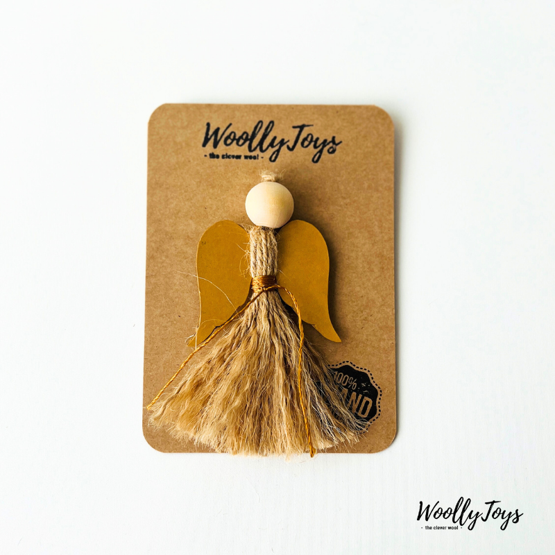 Egy kézműves natúr angyal karácsonyfadísz arany szárnnyal, spárgából és fából, elegáns kraft csomagoláson, készen az ajándékozásra.